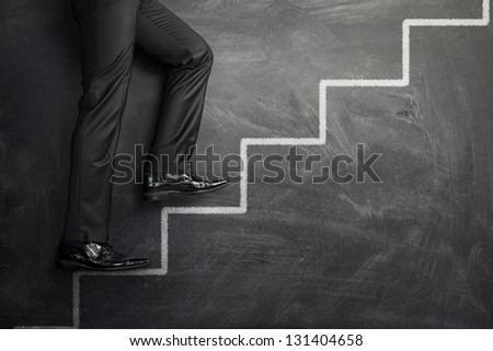 Businessman climbing the career stairs drawn on a chalkboard with copy space