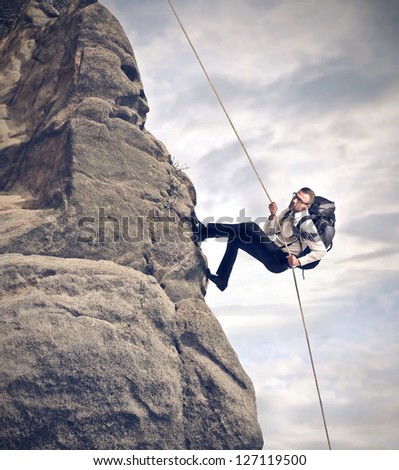 businessman climbing on mountain with rope and backpack
