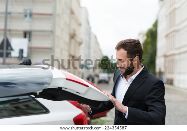 Businessman closing the\
boot of his car as he retrieves his belongings before leaving it in\
the parking lot