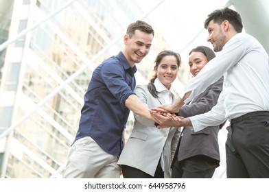 Businessman with colleagues stacking hand to cooperate on building background outdoor in city