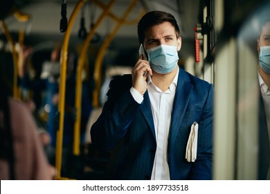 Businessman Communicating Over Cell Phone And Wearing Protective Face Mask While Commuting To Work By Bus During Coronavirus Pandemic. 