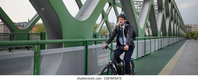 Businessman commuter on the way to work, riding bike over bridge, sustainable lifestyle concept. Wide shot. - Powered by Shutterstock