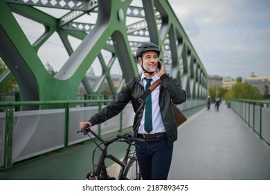 Businessman commuter on the way to work, pushing bike on bridge and calling on mobile phone, sustainable lifestyle concept. - Powered by Shutterstock