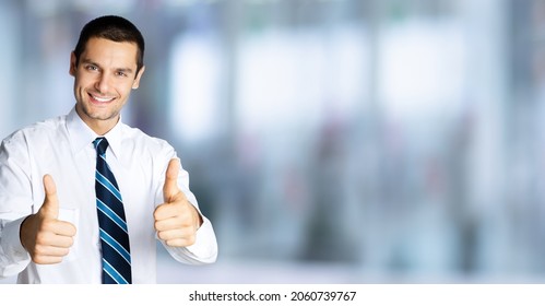 Businessman In Confident White Shirt And Tie, Showing Thumbs Up Like Hand Sign Gesture Blurred Modern Office Interior Background. Happy Smiling Man Gesturing. Success In Business. Male Executive Coach