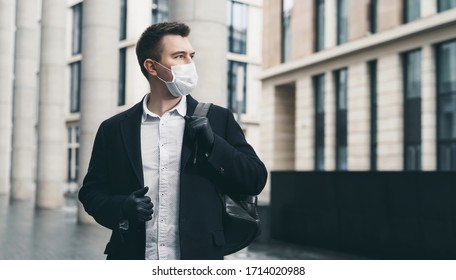 Businessman and coronavirus epidemic. Close up portrait of young business man in a disposable facial mask. A man defends himself against covid 19 on the big city street. Modern buildings at background - Powered by Shutterstock