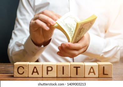 Businessman counts money on the background of the caption Capital. Capitalism, capital increase and influence. Financial liberalization of developing countries, unprincipled withdrawal of capital.