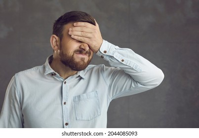 Businessman covers face with hand. Guy facepalms feeling ashamed of terrible mistake or poor memory. Annoyed guilty cringing business manager employee closes face with palm isolated on grey background