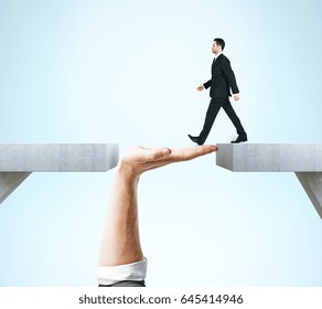 Businessman crossing abstract hand bridge on blue background. Teamwork concept