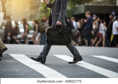 Businessman crossing the street on crosswalk and holding a laptop bag and smatphone in the city - Powered by Shutterstock