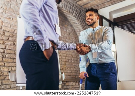 Businessman with a crutch at work shakes hands with his colleague