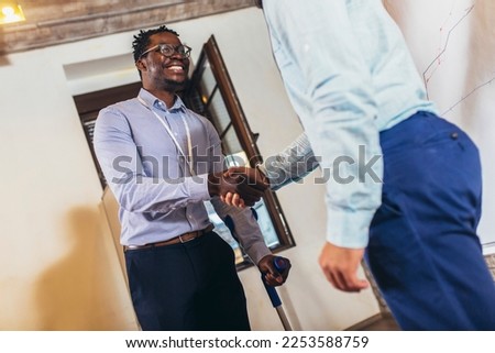 Businessman with a crutch at work shakes hands with his colleague