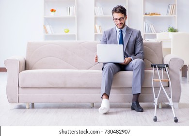 Businessman With Crutches And Broken Leg At Home Working