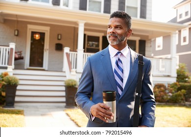 Businessman With Cup Of Coffee Leaving Suburban House For Work