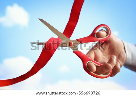 Businessman cutting a red ribbon with a pair of scissors at opening ceremony