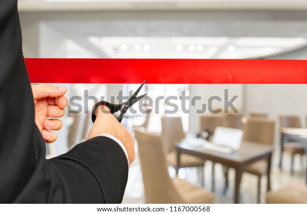 Businessman\
cutting red ribbon with pair of\
scissors