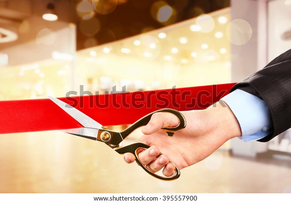 Businessman cutting red ribbon with pair of scissors\
close up