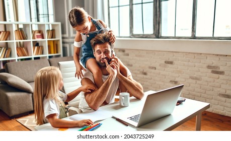 The businessman dad tries to work at the laptop when his little daughters play, fool around and interfere with him. Freelance, work from home. - Powered by Shutterstock