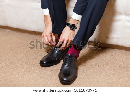 A businessman in dark blue suit, red socks and watches tying his