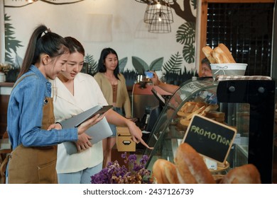 Businessman daughter coffee shop owner small business elderly woman retired Asian pensioner holding tablet Receive orders customer bakery cabinet Asian woman white shirt Mother counting money counter. - Powered by Shutterstock