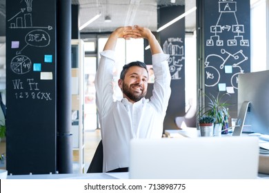 Businessman At The Desk In His Office Stretching Arms.