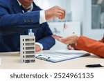  A businessman at a desk in a sales office sells a condo building to a customer. They agree to sign a contract, covering real estate investments in offices, apartments, and commercial properties.