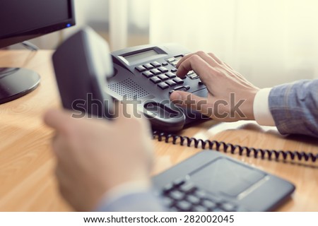 businessman dialing voip phone in the office, keyboard and monitor detail in the background with vintage color tone effect