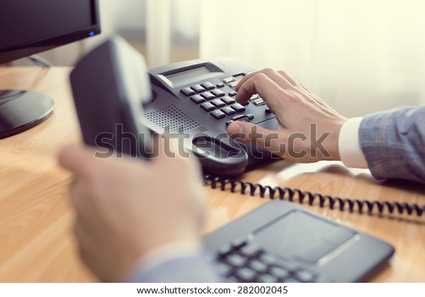 businessman\
dialing voip phone in the office, keyboard and monitor detail in\
the background with vintage color tone\
effect