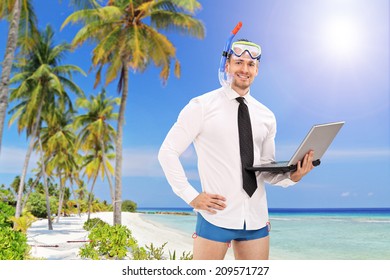 Businessman With A Diving Mask Holding A Laptop And Standing On A Beach With Palm Trees