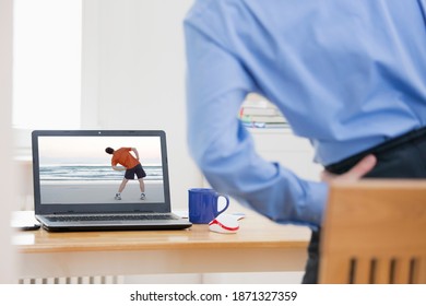 Businessman Doing Stretching Exercise In Front Of Laptop While Working From Home - Same Model On The Screen And In The Foreground