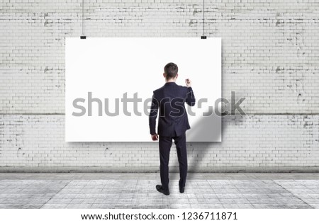 Businessman drawing on white backdrop against white brick wall