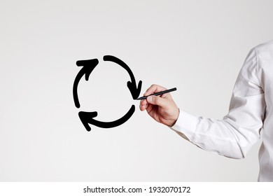 Businessman draws a recycling circle with arrows on gray background. Business or economic stagnation or recycle concept.