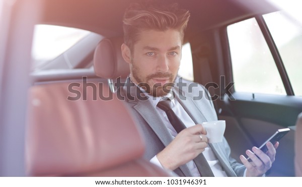 Businessman\
drinking coffee in car with phone in\
hand