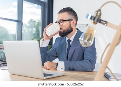 businessman drinking coffee while working at workplace with laptop in office