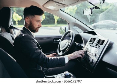 Businessman Driving A Car Turns On The Music In The Car Player, A Man Before A Trip In A Business Suit