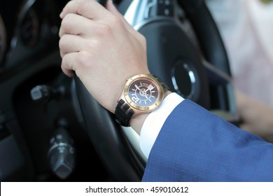 Businessman driving his car, hand on the steering wheel. Hand with golden watch. Business concept.