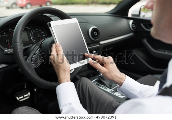 Businessman\
driving his expensive car and connecting with a digital tablet, he\
is using mobile apps and GPS, car\
interior