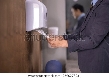 Businessman is drying his hands using paper towels from a dispenser in a modern office restroom
