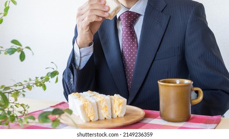 A Businessman Eating A Sandwich. Egg Salad Sandwich And Coffee.