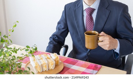 A Businessman Eating A Sandwich. Egg Salad Sandwich And Coffee.