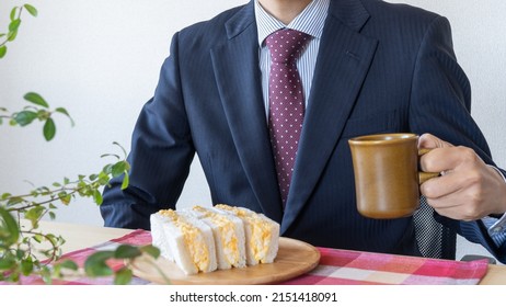 A Businessman Eating A Sandwich. Egg Salad Sandwich And Coffee.