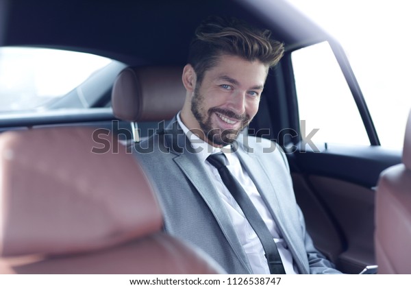 Businessman in elegant\
suit on backseat of\
car