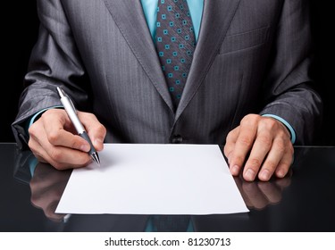 Businessman In Elegant Suit Working With Documents Sign Up Contract, Business Plan Sitting At Desk Working, Concept Of Hold Blank, Empty Sheet Of White Paper Over Black Background.