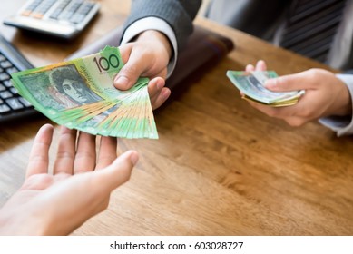 Businessman as an employer paying cash (australian dollar money) to worker at the office - wage, loan and bribery concepts