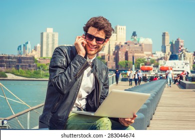 Businessman enjoying working outside. Wearing leather jacket, sunglasses, a guy with beard, sitting on bench at harbor, working on laptop computer, talking on phone in the same time. Instagram effect. - Shutterstock ID 283044674