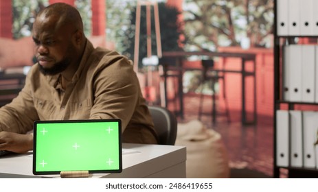 Businessman examines annual sales reports on documents next to a green screen tablet display, doing an accounting analytics plan. Entrepreneur working remotely from home office. Camera A. - Powered by Shutterstock