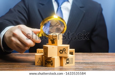 A businessman examines boxes goods with magnifying glass. Market structure research, find unoccupied target consumer niches, demand assessment. Marketing sales promotion strategy. Retailer