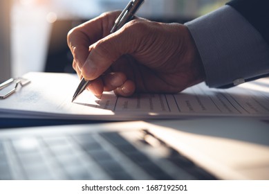 Businessman, executive manager hand filling paper business document, signing contract, partnership agreement and working on laptop computer on desk in modern office, close up