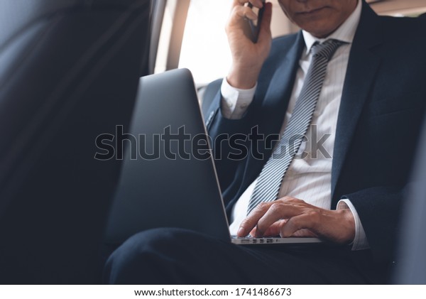 Businessman, executive manager working on laptop\
computer and calling via  mobile smart phone inside a car, portable\
office, business concept. Corporate man, lawyer going to workplace,\
close up