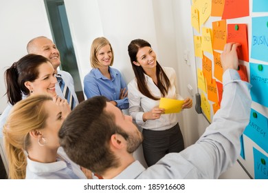 Businessman Explaining Labels On Whiteboard To Colleagues In Meeting