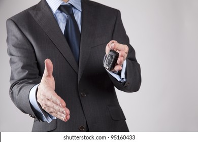 A businessman extending car key and holding out his hand to shake, isolated on greybackground - Shutterstock ID 95160433